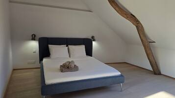 Et soveværelse med en seng, knægt, vægmonteret lampe og en træbjælke.