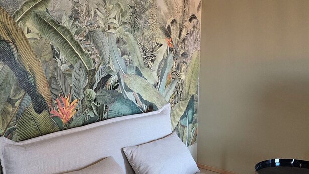 A room with a sofa, a small round table, and a mural of tropical foliage on the wall.