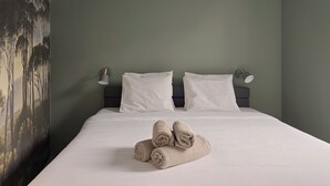 A neatly made bed with white linens and two rolled towels on the bed.