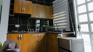 Una cocina moderna con armarios negros y de madera, electrodomésticos de acero inoxidable y un ventanal con persianas.
