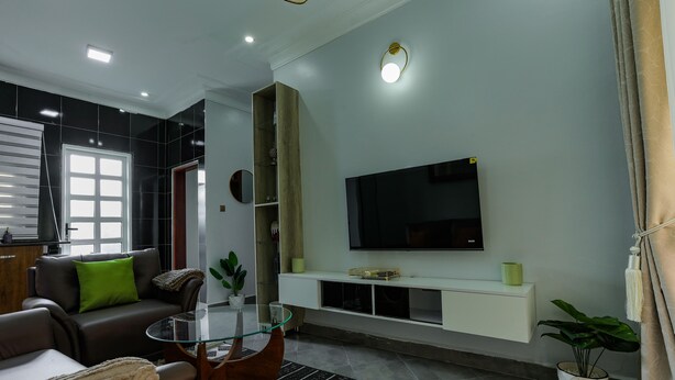 Una sala de estar moderna con un sofá, una mesa de centro de vidrio, un televisor de pantalla plana montado en una pared blanca y un mueble empotrado para entretenimiento.