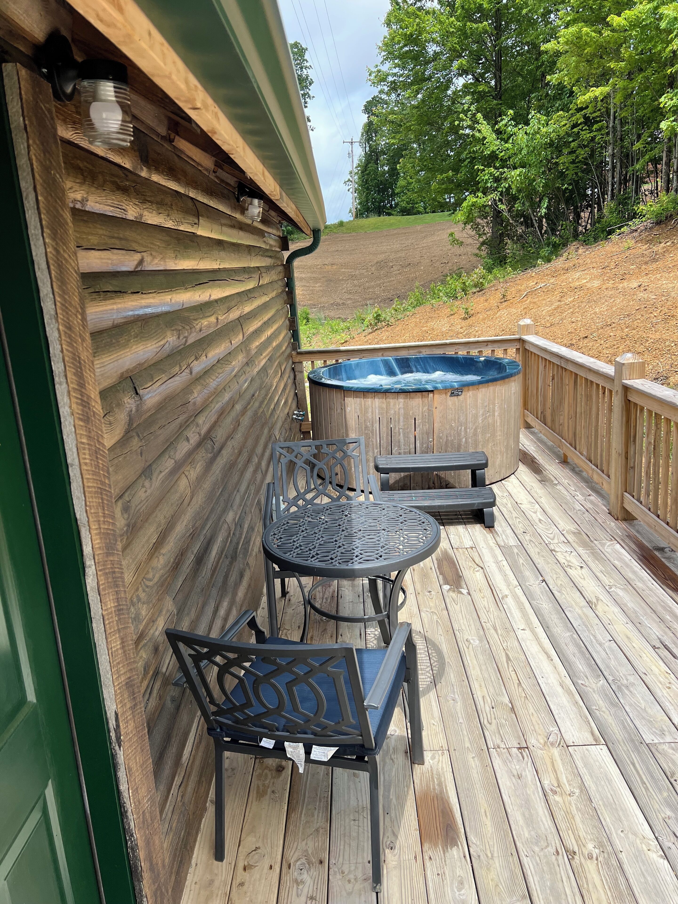 A wooden deck with a hot tub, two chairs, and a table.