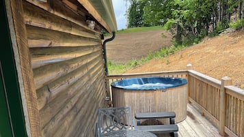 A wooden deck with a hot tub, two chairs, and a table.