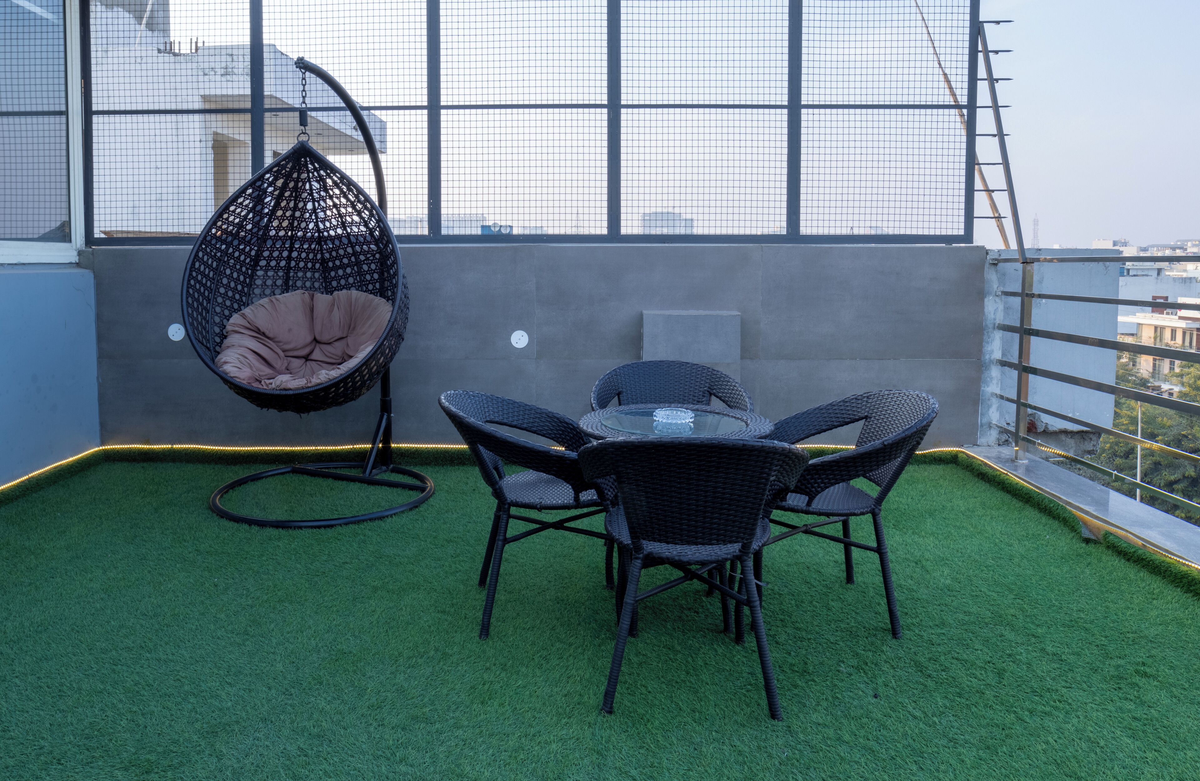 A rooftop terrace with artificial grass, a hanging chair, and a table with chairs.