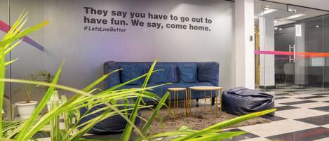 A modern office lobby with a blue sofa, a small table, and a bean bag. There's a motivational quote on the wall and a glass door in the background.