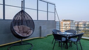 A rooftop terrace with a hanging chair, wicker chairs, and a small table.