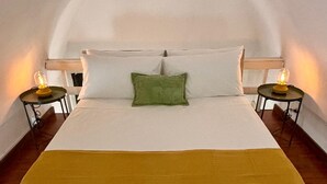 A bed with white linens, a green pillow, and a mustard-colored throw blanket. There are two bedside tables with lamps.