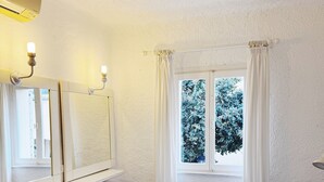 A bedroom with a bed, two stools, a mirror, and a window with curtains.