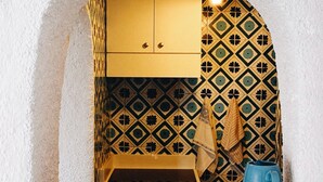 A kitchen with a white textured wall, a patterned backsplash, a wooden cabinet, a blue mug, and a towel hanging on the wall.