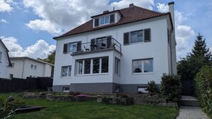 A two-story house with a balcony, a stone wall, and a grassy yard. - Large apartment in a prime location in Bad Salzuflen (Bad Salzuflen)