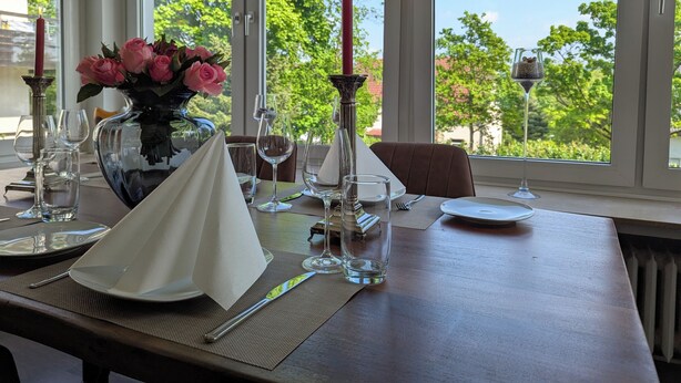 A dining table set for two with a vase of pink roses, wine glasses, and a candle. - Large apartment in a prime location in Bad Salzuflen (Bad Salzuflen)