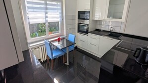 A modern kitchen with white cabinets, a black countertop, and a window with blinds. - Large apartment in a prime location in Bad Salzuflen (Bad Salzuflen)