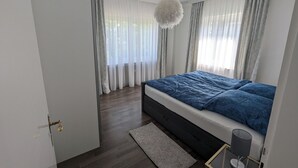 A modern bedroom with a large bed, a hanging light fixture, and sheer curtains. - Large apartment in a prime location in Bad Salzuflen (Bad Salzuflen)