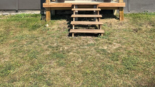 Eine hölzerne Veranda mit einer weißen Tür, zwei Blumentöpfen und einer Treppe aus Holz, die zur Tür hinaufführt.