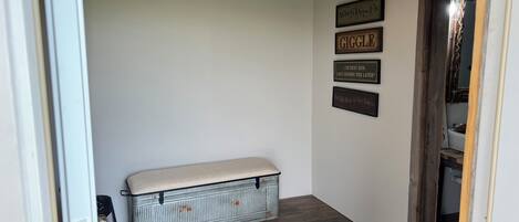 A hallway with a bench, wooden flooring, and a wall with framed sayings.