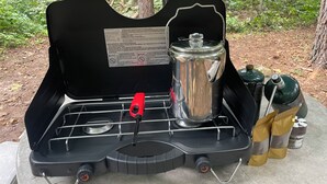 A portable camping stove with a pot on it, placed on a table outdoors.