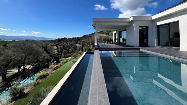 Une maison moderne dotée d’une grande piscine, d’un patio couvert et offrant une vue sur la campagne.