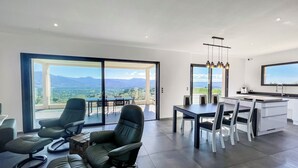 Un salon moderne avec un coin repas, de grandes portes-fenêtres coulissantes donnant sur un balcon avec vue sur les montagnes.