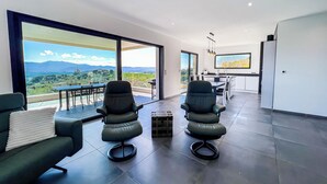Un salon moderne avec deux fauteuils noirs, un canapé et une grande fenêtre offrant une vue panoramique.