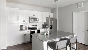 Una cocina moderna con armarios blancos, electrodomésticos de acero inoxidable y una isla central con taburetes de bar.