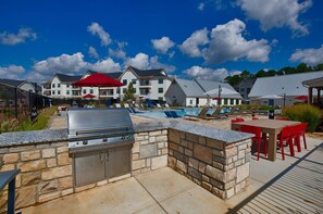 A poolside area with a barbecue grill, outdoor seating, and a view of residential buildings.