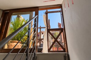 Eine Treppe mit Metallgeländer führt zu einem Fenster mit Blick auf ein Gebäude und eine Zimmerpflanze.