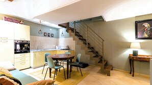 A compact kitchen with a dining area, a sofa, and a staircase. - La Serenissima: 2BR Castello Apartment, Private Roof Terrace, 3 min to San Marco (Venezia)
