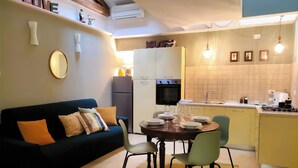 A compact living space with a sofa, dining table, chairs, kitchen area, and a built-in oven. - La Serenissima: 2BR Castello Apartment, Private Roof Terrace, 3 min to San Marco (Venezia)