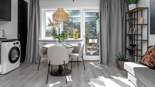 A modern living room with a dining area, a washing machine, and a large window with curtains.