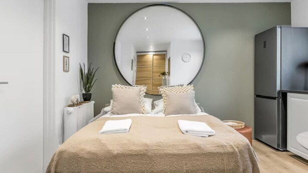 Un dormitorio moderno con una cama grande, un espejo redondo, un refrigerador y una planta en maceta.