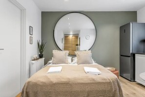 Ein modernes Schlafzimmer mit einem großen Bett, einem runden Spiegel, einem Kühlschrank und einer Topfpflanze.