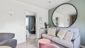 Una sala de estar moderna con un sofá gris, un espejo redondo y un otomano rosa.