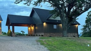A two-story house with a stone foundation and dark siding, a covered porch, and a gravel driveway.