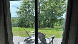 A room with a large sliding glass door leading to an outdoor deck with two Adirondack chairs and a patterned rug.