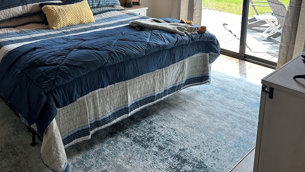 A bedroom with a large bed, a nightstand, a lamp, and a view of the outdoors.