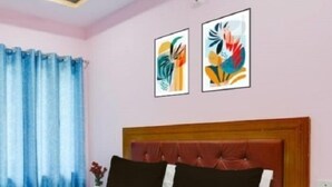 Une chambre d’hôtel avec un lit, une tête de lit, des rideaux et deux œuvres d’art encadrées accrochées au mur.
