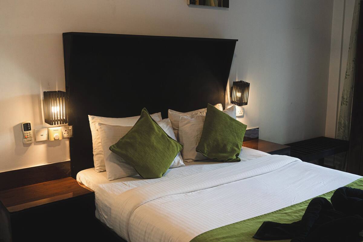 Een hotelkamer met een groot bed, een nachtkastje, een schilderij aan de muur en een lamp.