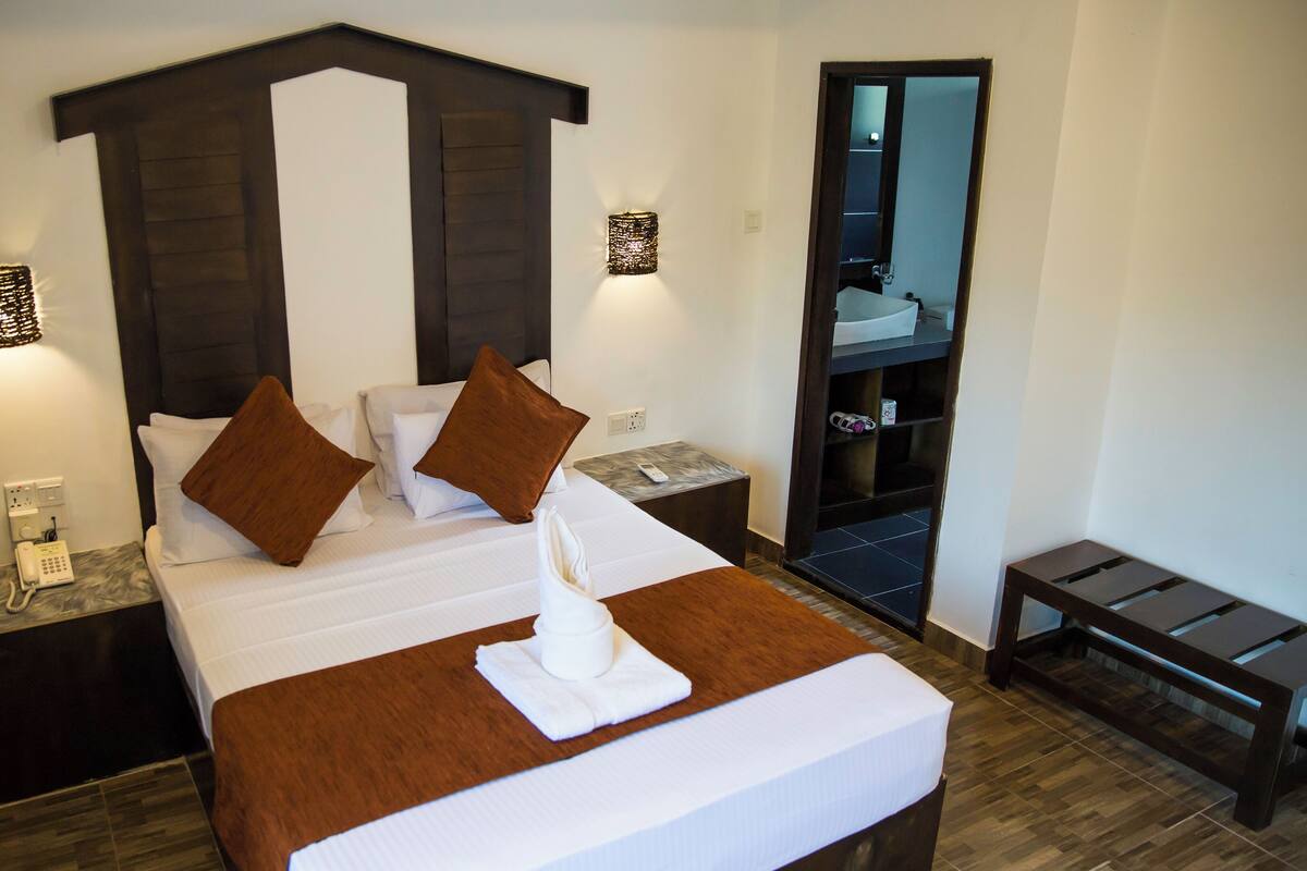 Een hotelkamer met een groot bed, twee nachtkastjes, een bijzettafeltje, een spiegel en een houten bank.