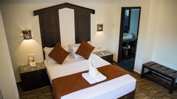 Habitación de hotel con una cama grande, dos mesitas de noche, un tocador, un espejo y un banco de madera.