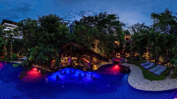 Een nachtzicht van een resort met een groot zwembad, ligbedden en een houten terras.