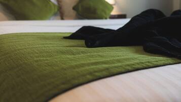 A neatly made bed with a green throw blanket and pillows, a bedside lamp, and a painting on the wall.