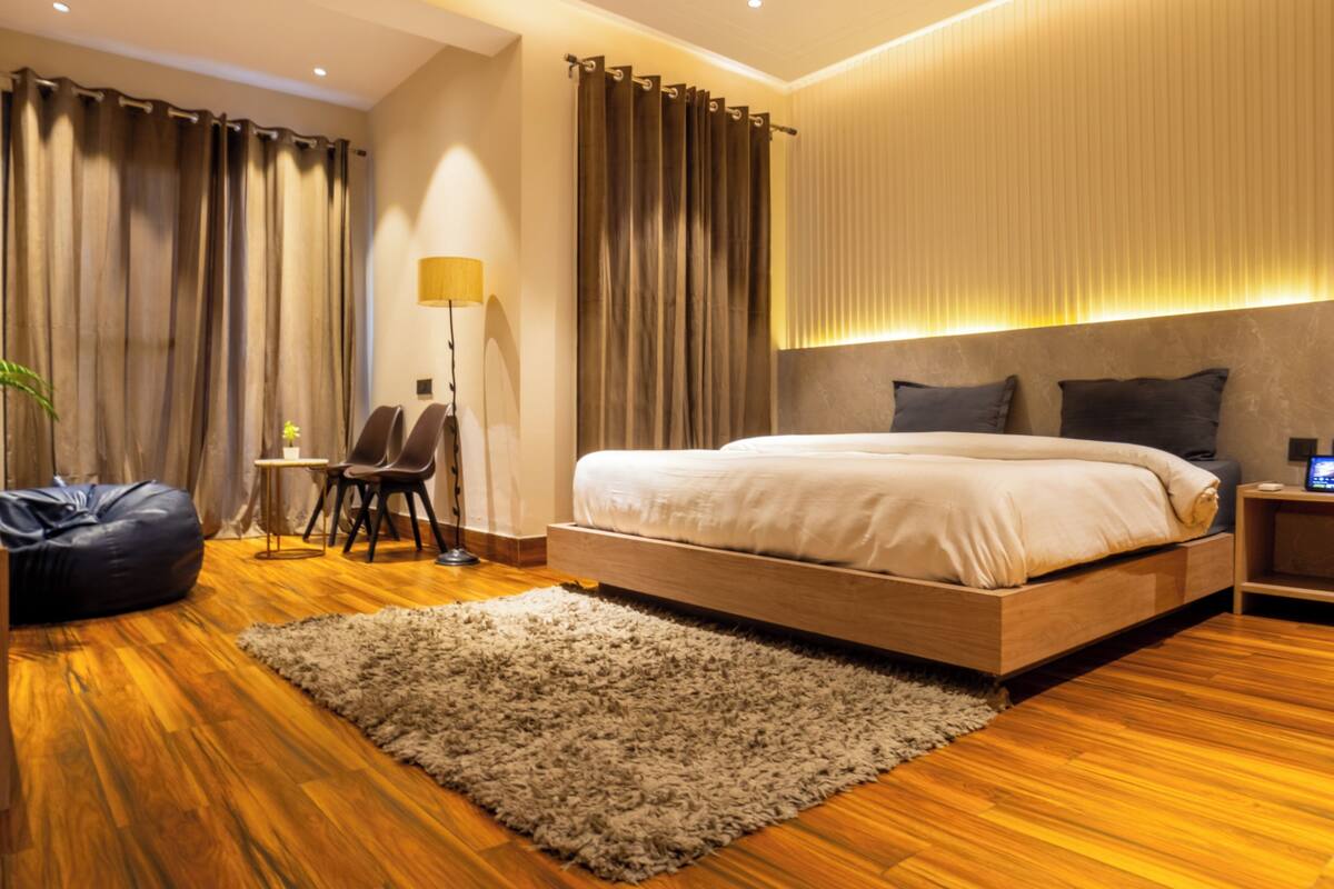 A modern bedroom with a large bed, wooden flooring, a small desk, and a chair.