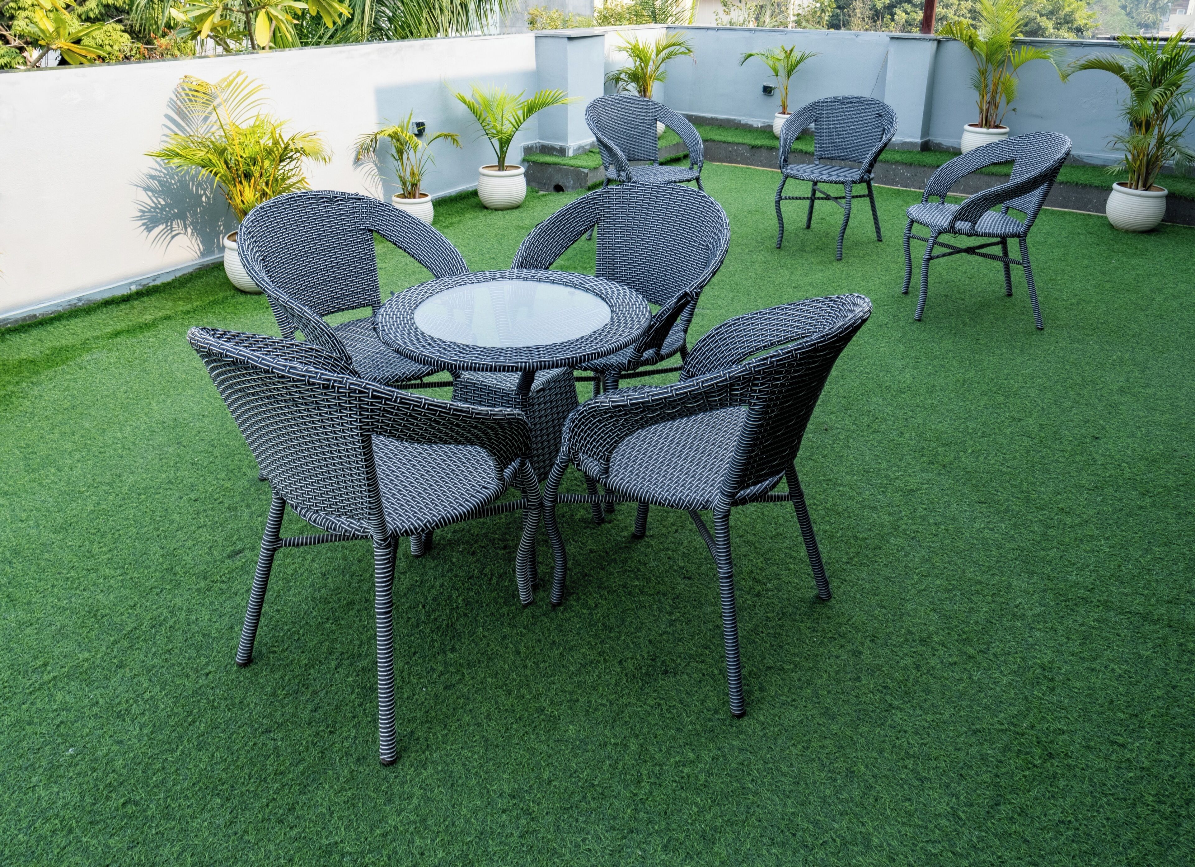 A patio with a round table and six wicker chairs, surrounded by artificial green grass.