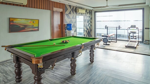 A pool table with balls, a treadmill, and exercise equipment in a room with large windows. - Housr Golf Course Road Phase 1 Metro (Gurugram)