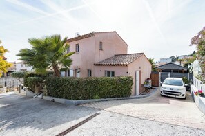 Ein zweistöckiges Haus mit einem Ziegeldach, einem weißen Auto auf der Auffahrt und einer Palme im Vorgarten.