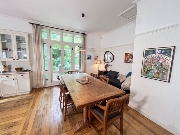 Un comedor con una mesa y sillas de madera, un mueble con puertas de vidrio y vistas a zonas verdes a través de amplios ventanales.