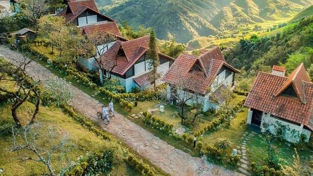 Une rangée de maisons traditionnelles aux toits inclinés, entourées d’une végétation luxuriante et avec des collines en arrière-plan.