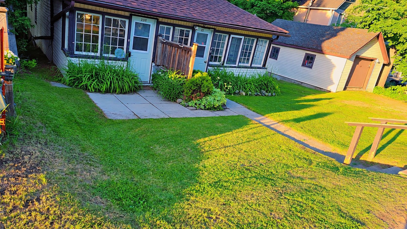 A residential house with a well-maintained lawn, a wooden deck, and a small shed.