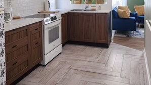 Uma cozinha moderna com armários brancos, bancada de madeira e piso em padrão herringbone.
