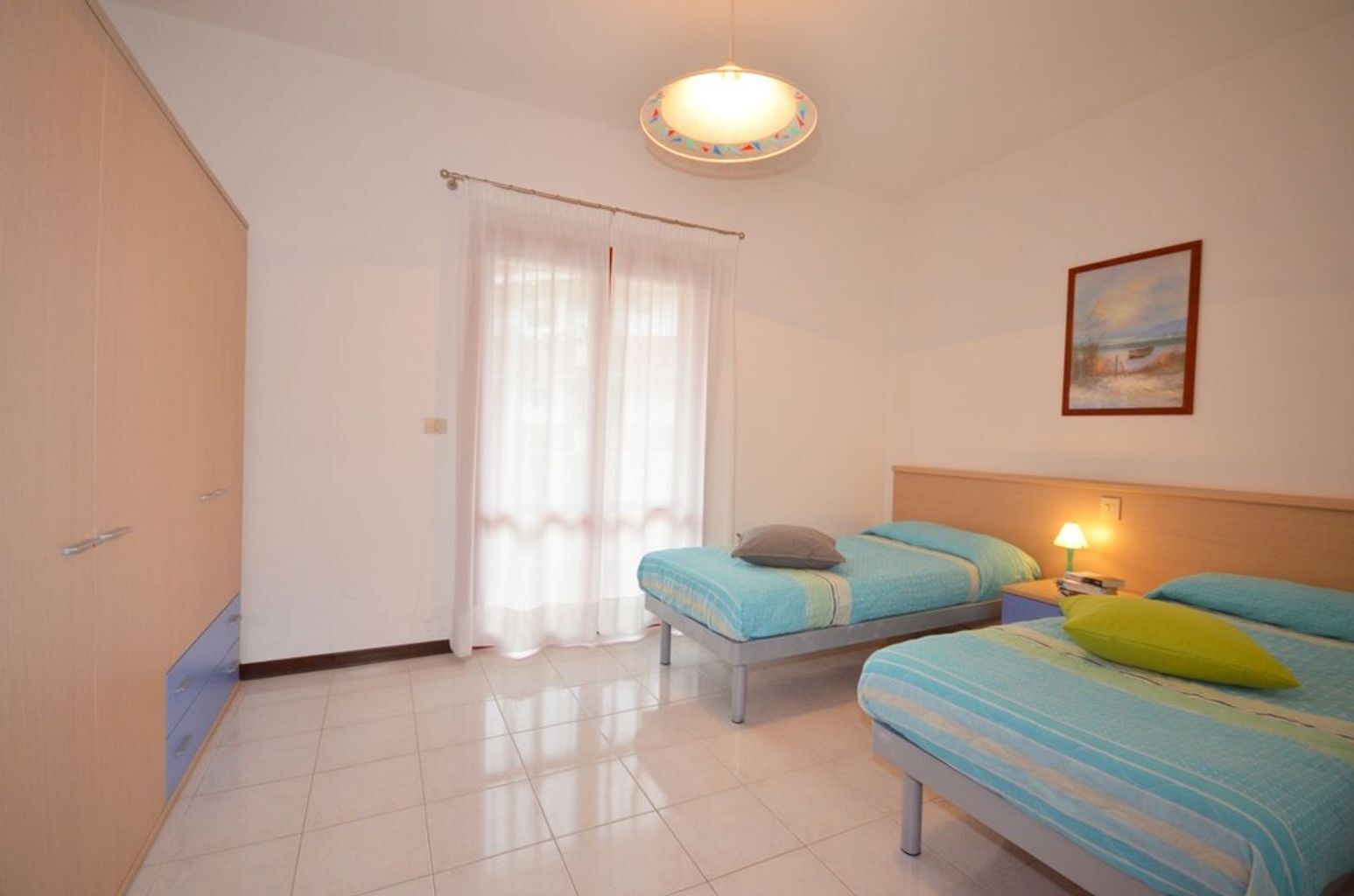 Quarto com duas camas, mesa de cabeceira, abajur, quadro na parede e janela com cortinas.